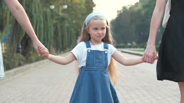 Mom and her small daughter with long hair walking together holding hands in summer park.