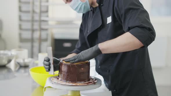 Side View of Unrecognizable Man in Coronavirus Face Mask Spreading Chocolate Topping on Cake on
