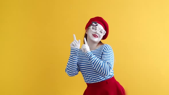 A female mime with a white face, striped T-shirt and beret dances pointing her fingers up