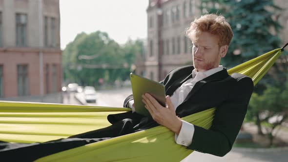 Young Businessman Using Tablet for Work in Hammock Outdoors