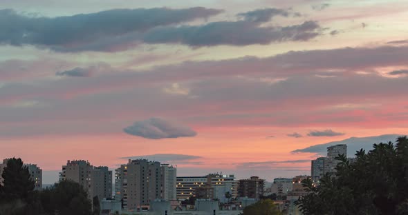 Timelapse of red and pink cloudsing fast during sunset over a view of apartment buildings and hotels