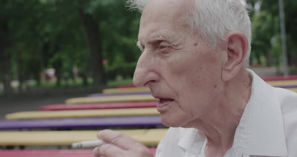 Portrait of Thoughtful Grandfather Smoking Cigarette and Talking in Park