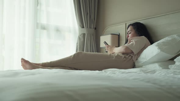 Thoughtful Young Caucasian Woman Using Smartphone While Sitting on Bedroom