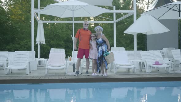 Happy Mature Couple Standing at the Swimming Pool Hugging Their Little Granddaughter