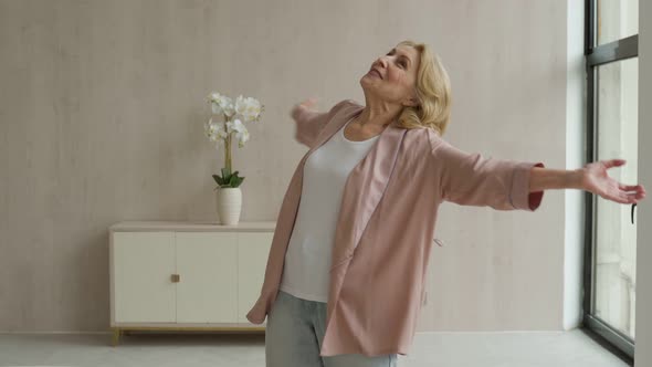 A Cheerful Elderly Woman Listens to Music and Dances in Her Living Room