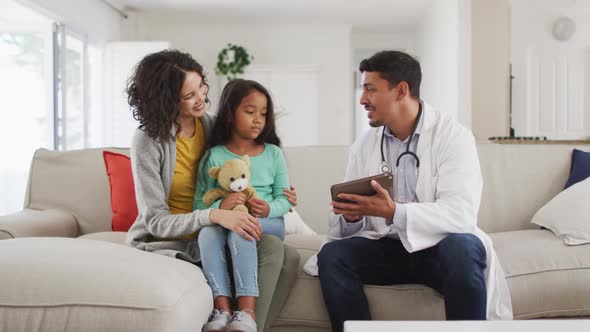 Hispanic male doctor talking to mother and daughter at home, all wearing face masks