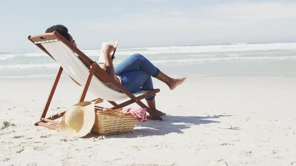 African american woman reading and lying on sunbed on sunny beach