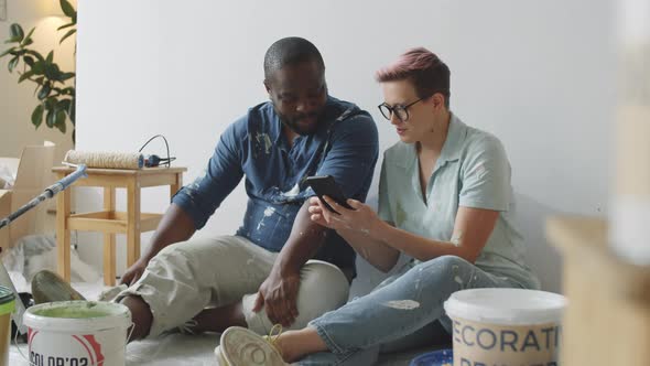 Diverse Couple Using Smartphone on Break in Room under Renovation