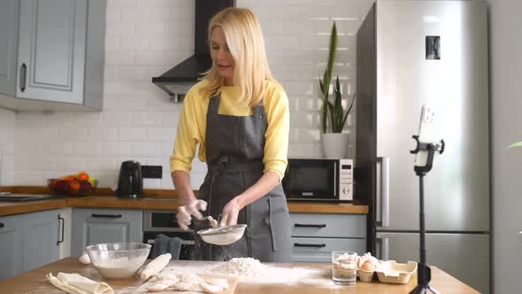 Positive Middleaged Woman in Apron Preparing a Dough and Streaming It in Social Media