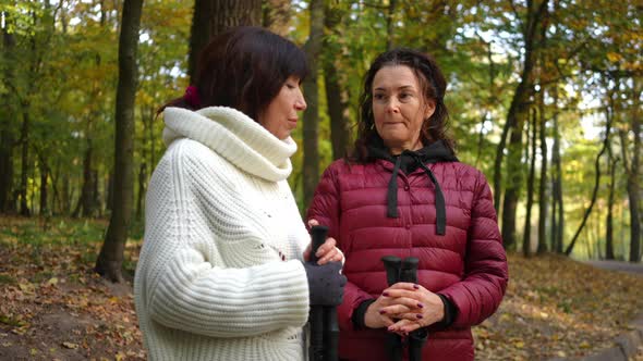 Thoughtful Focused Mature Woman Talking with Friend Standing in Autumn Park with Ski Poles