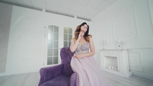 Beautiful bride in wedding dress admires herself while sitting on the chair in a room.