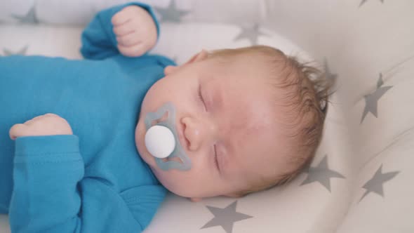 Newborn Baby with Pacifier Sleeps in Cocoon in Rocking Crib