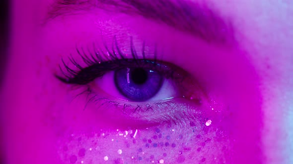 Closeup of Young Woman Eye Wearing Decorative Lenses in Ultraviolet Light Makeup with Glitter and