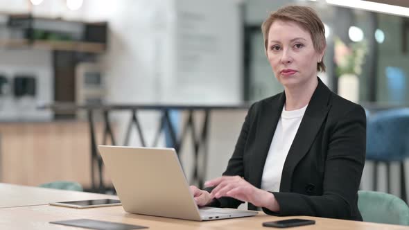 Old Businesswoman with Laptop Pointing at the Camera 