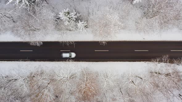 Two cars are driving over a winter road from left to right, top-down drone shot.