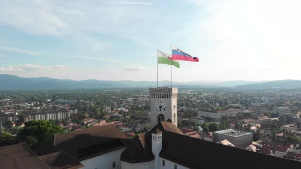 Slow drone flying up with a view of Ljubljana city above the castle with the flag of the city and a