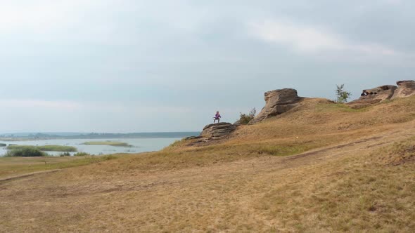 A Girl is Doing Fitness on a Hill on the Lake Shore