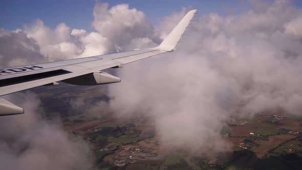 Airplane Wing in the Sky Over Fields and Buildings Through the Clouds