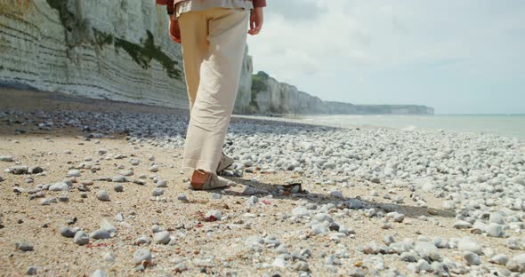 A Young Woman Walks Along a Pebbly Beach Past Sheer Chalk Cliffs