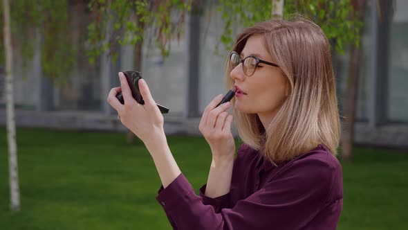 Attractive Caucasian woman draws her lips with lipstick looks