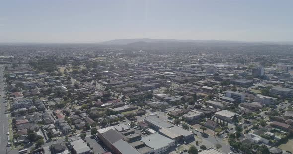 Sideways aerial pan over Grater City of Dandenong on clear summers day. Buses moving along suburban