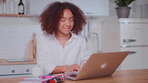 Young Happy African American Business Woman Typing Email in Laptop Sits at Kitchen