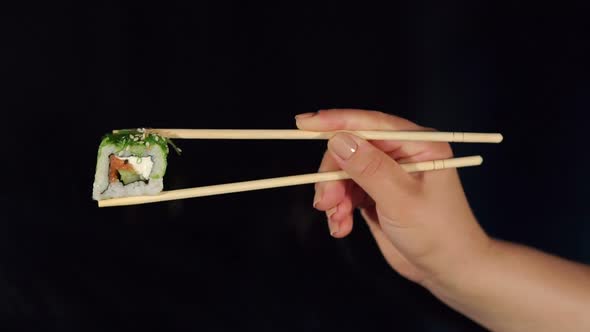 Girl Holding Sushi By Chopsticks on Black