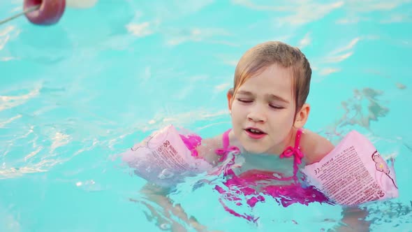 a Funny Little Girl Swims in Inflatable Armbands in a Pool Near the Buoys