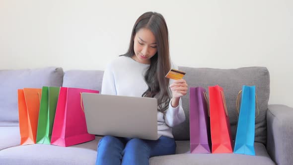 While shopping from home, a young woman holds up her credit card as she inserts the numbers into her