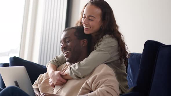 Relaxed Young Couple At Home Sitting On Sofa Browsing Internet On Laptop Computer