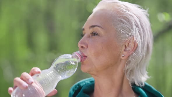 Headshot of Satisfied Senior Sportswoman Drinking Refreshing Water in Sunlight Outdoors
