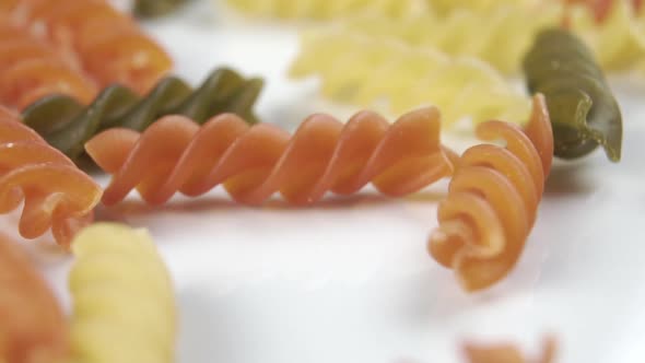 Pouring multicolored uncooked Italian spiral pasta on a white plate