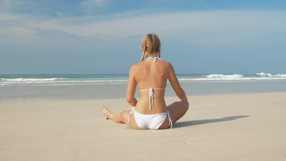 Strong Girl on Sand Holds Leg and Enjoys Ocean Waves