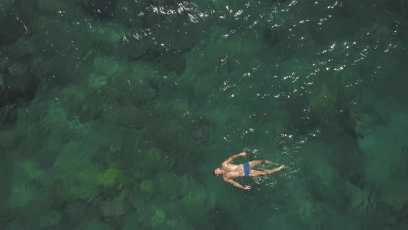 Aerial View of Sexy Young Man in Blue Swim Shorts Swimming and Floating in Ocean