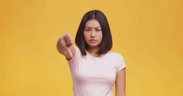 Dislike Concept. Young Dissatisfied Asian Woman Gesturing Thumb Down, Orange Background