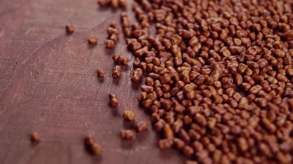 Roasted buckwheat tea grains on a dark brown rustic wooden board surface. Macro