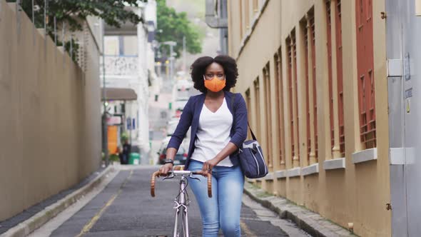 African american woman wearing face mask carrying bicycle in street