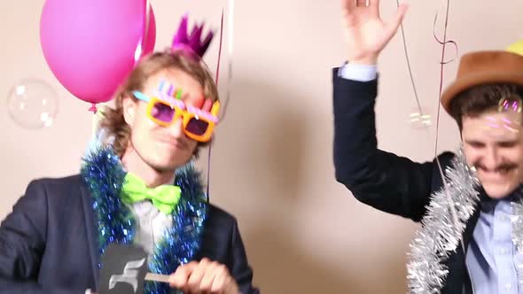 Two men holding sign in love and dancing in photo booth