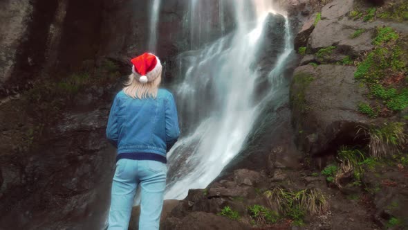 girl in Santa Claus hat stands on waterfall on Christmas Day. Enjoying nature