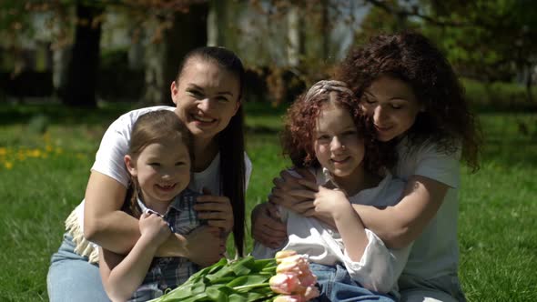 Two Women with Their Daughters are Sitting in the Park on the Grass