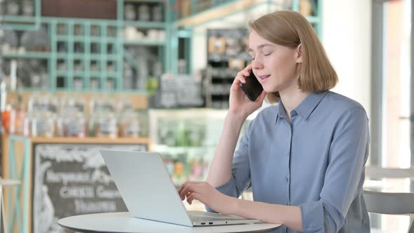 Young Woman Talking on Smartphone While Using Laptop