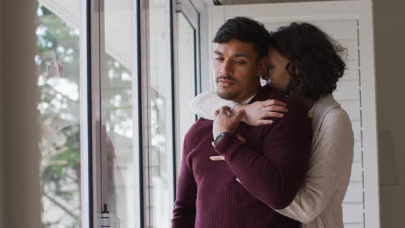 Romantic hispanic couple embracing cuddling standing in window