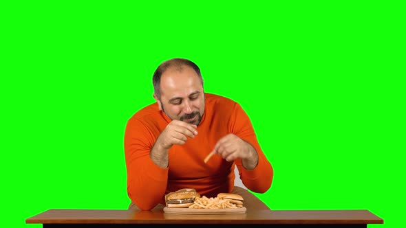 Funny Adult Man at a Table with a Plate of Fast Food Eats Many French Fries, Then Leaves Away. Green