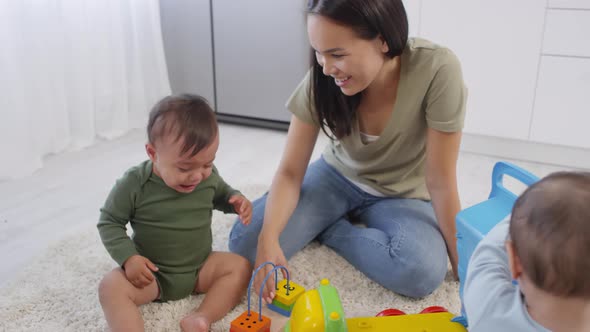 Asian Mom Comforting Crying Toddler and Sibling Playing