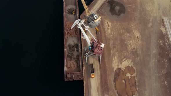 Huge Harbor Cranes on the River Bank Unload Rubble From a Barge