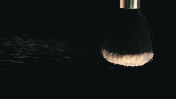 Cosmetic Powder for the Face is Poured From a Brush on a Black Background