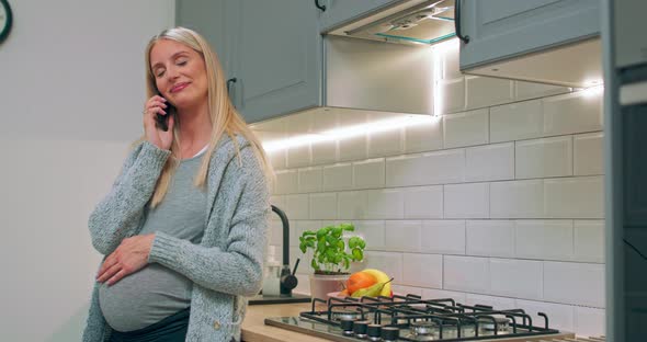 Young Happy Pregnant Woman Talking on Mobile Phone with Husband at Kitchen