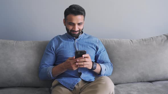 Happy Smiling Millennial Indian Man in Causal Jeans Shirt Using Mobile App