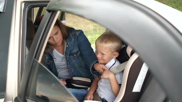 Closeup of Mother Fastens Her Little Son's Seat Belts in a Car Seat in the Car