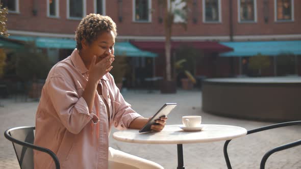 Excited African Woman Looking at Digital Tablet Screen in Outdoors Coffee Shop